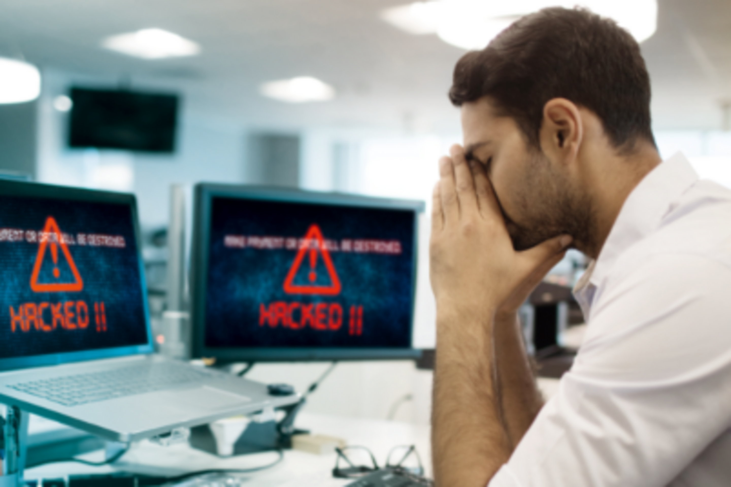 Angestellter sitzt vor Hacker-Nachricht am Bildschirm und vergräbt sein Gesicht in seinen Händen.