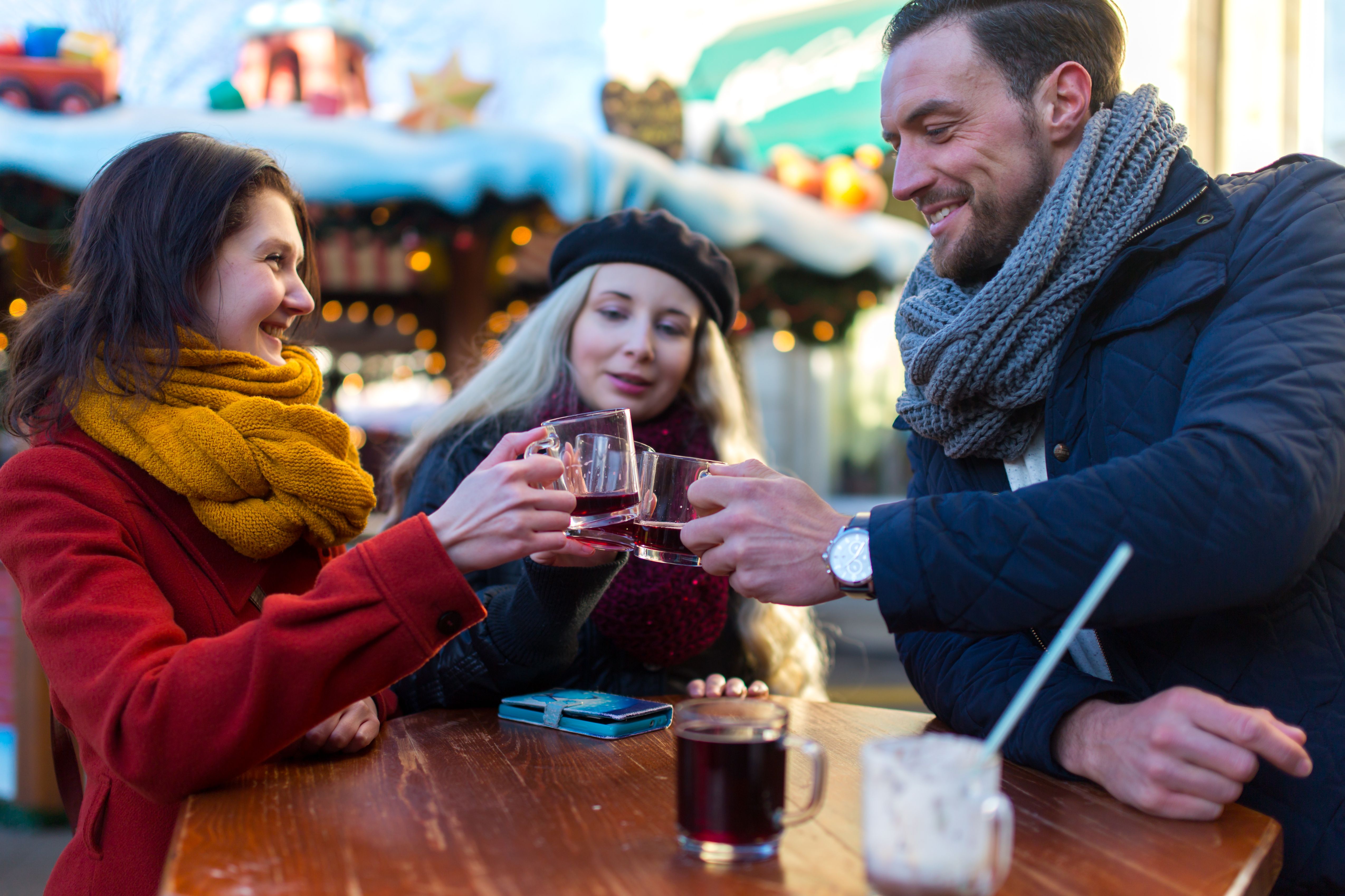 Zwei Frauen und ein Mann stossen an einem Weihnachtsnachtsmarkt mit Glühwein an