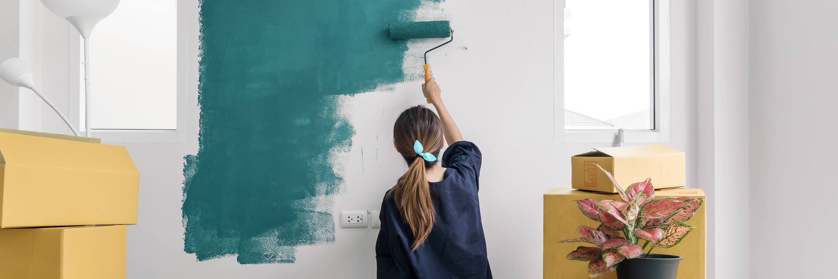 Woman is moving and painting a wall in colors of Green