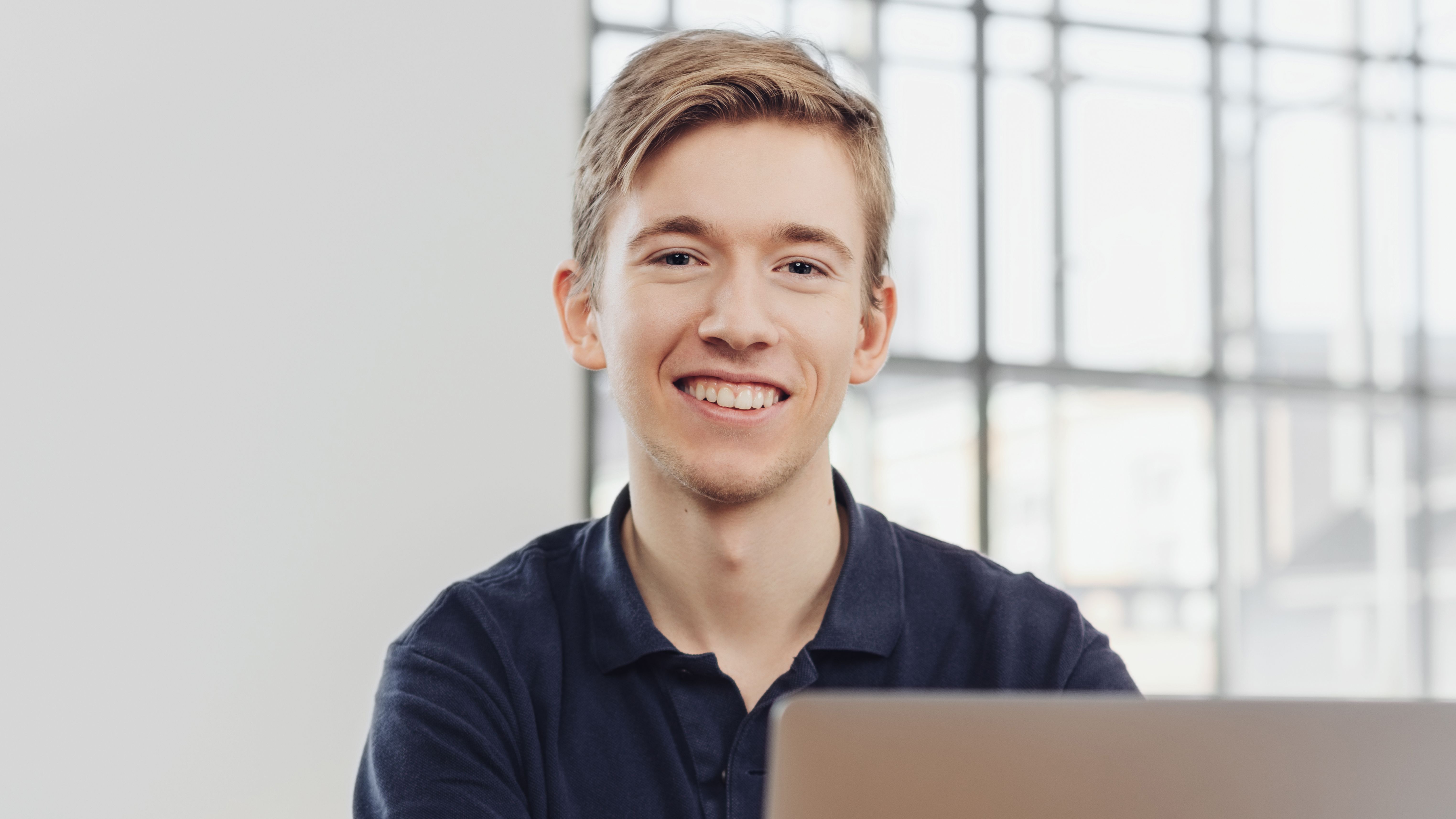 Lachender Jugendlicher am Laptop am Arbeitsplatz