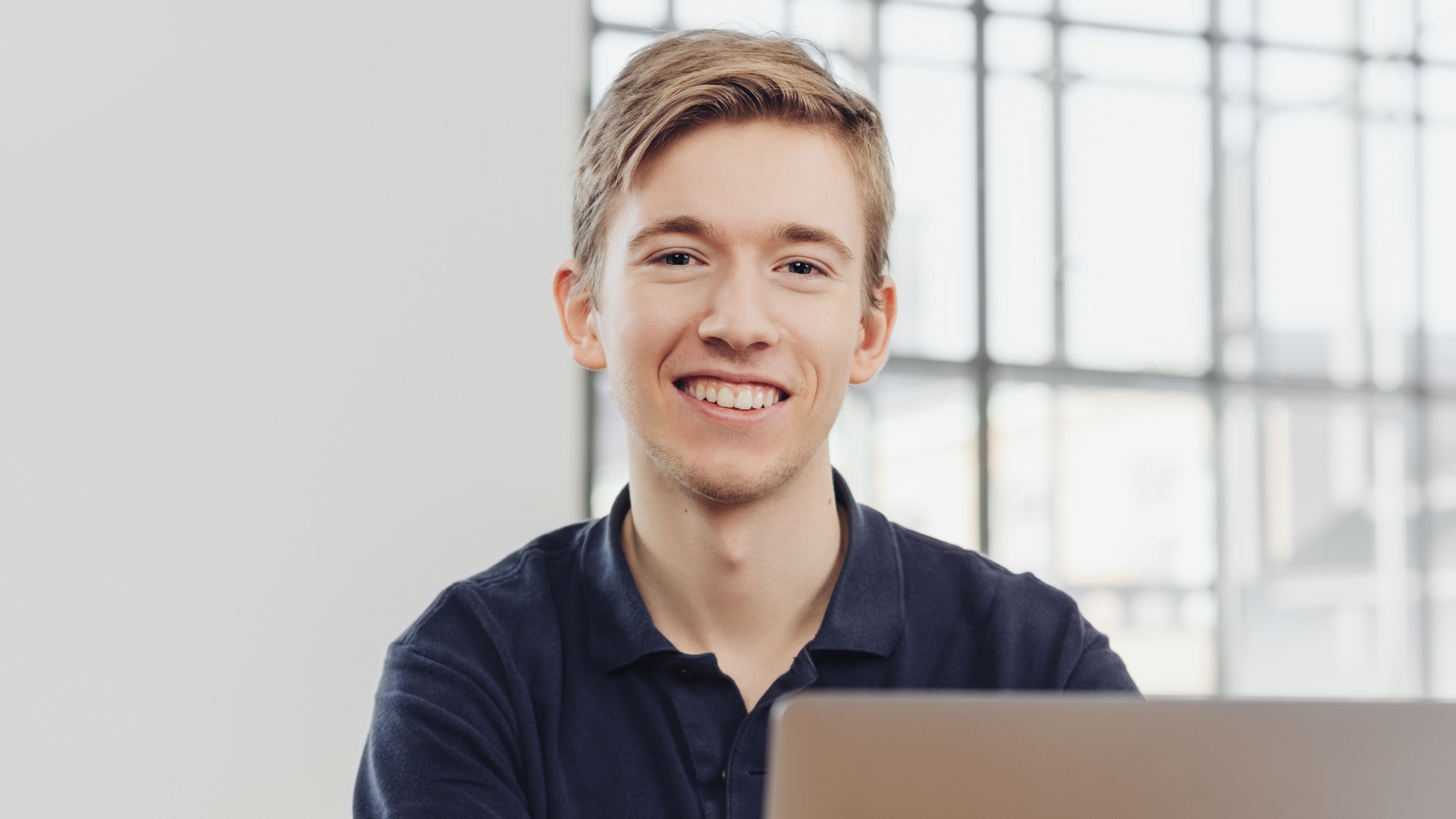 Lachender Jugendlicher am Laptop am Arbeitsplatz