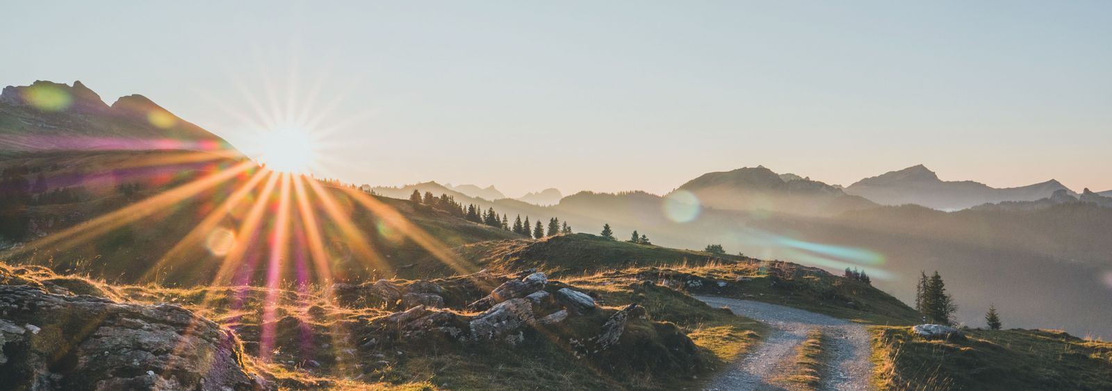Sonnenaufgang über einer alpinen Berglandschaft mit einem Schotterweg im Vordergrund