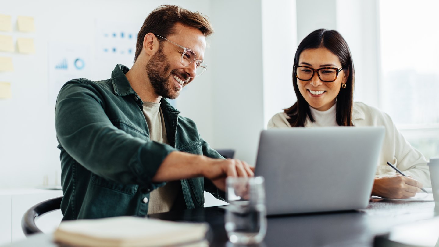 A man and a woman discussing something while pointing at a laptop.
