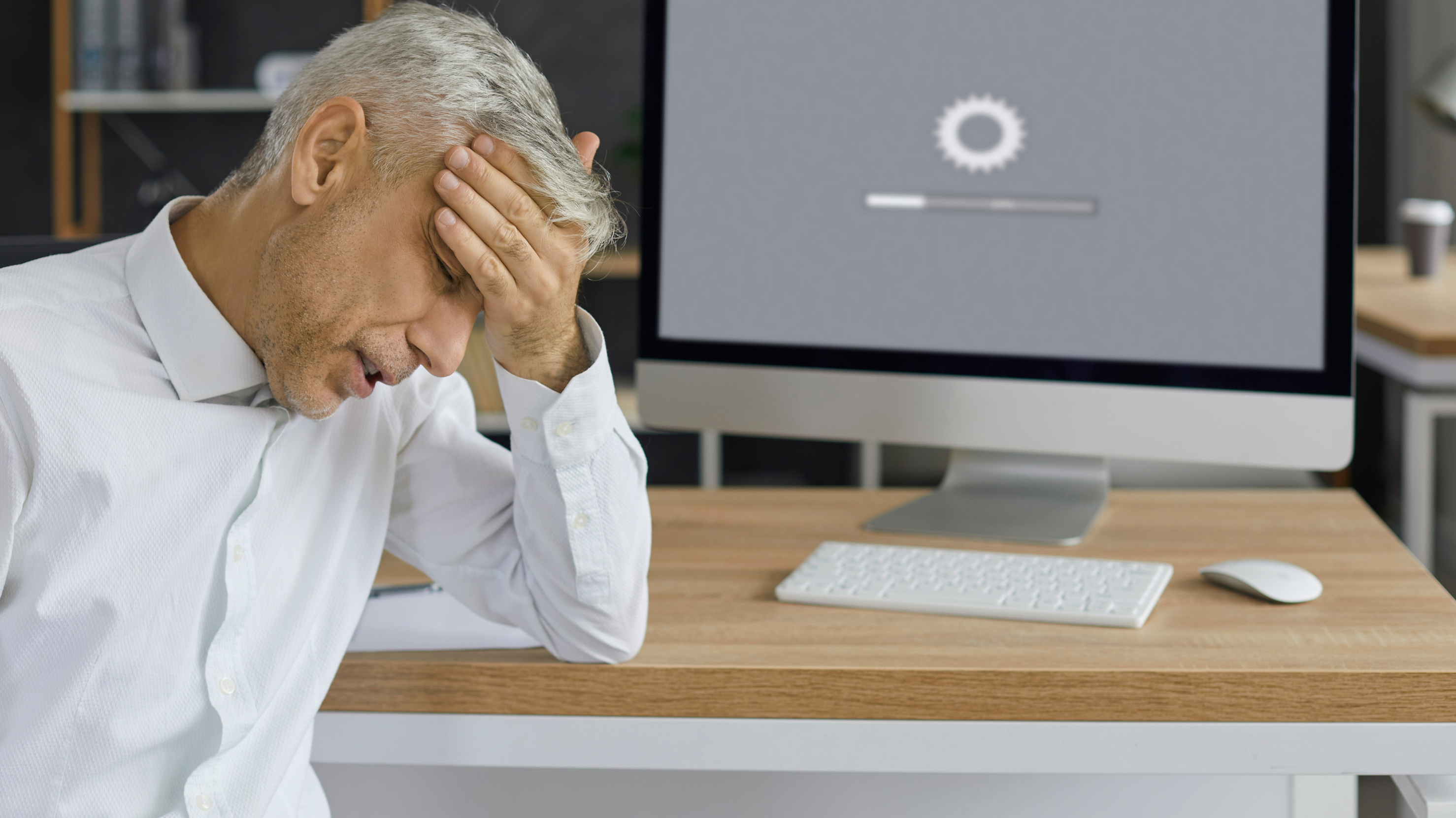 Frustrated man in an office sitting in front of a computer with a slow-loading screen – symbolic of poor website performance