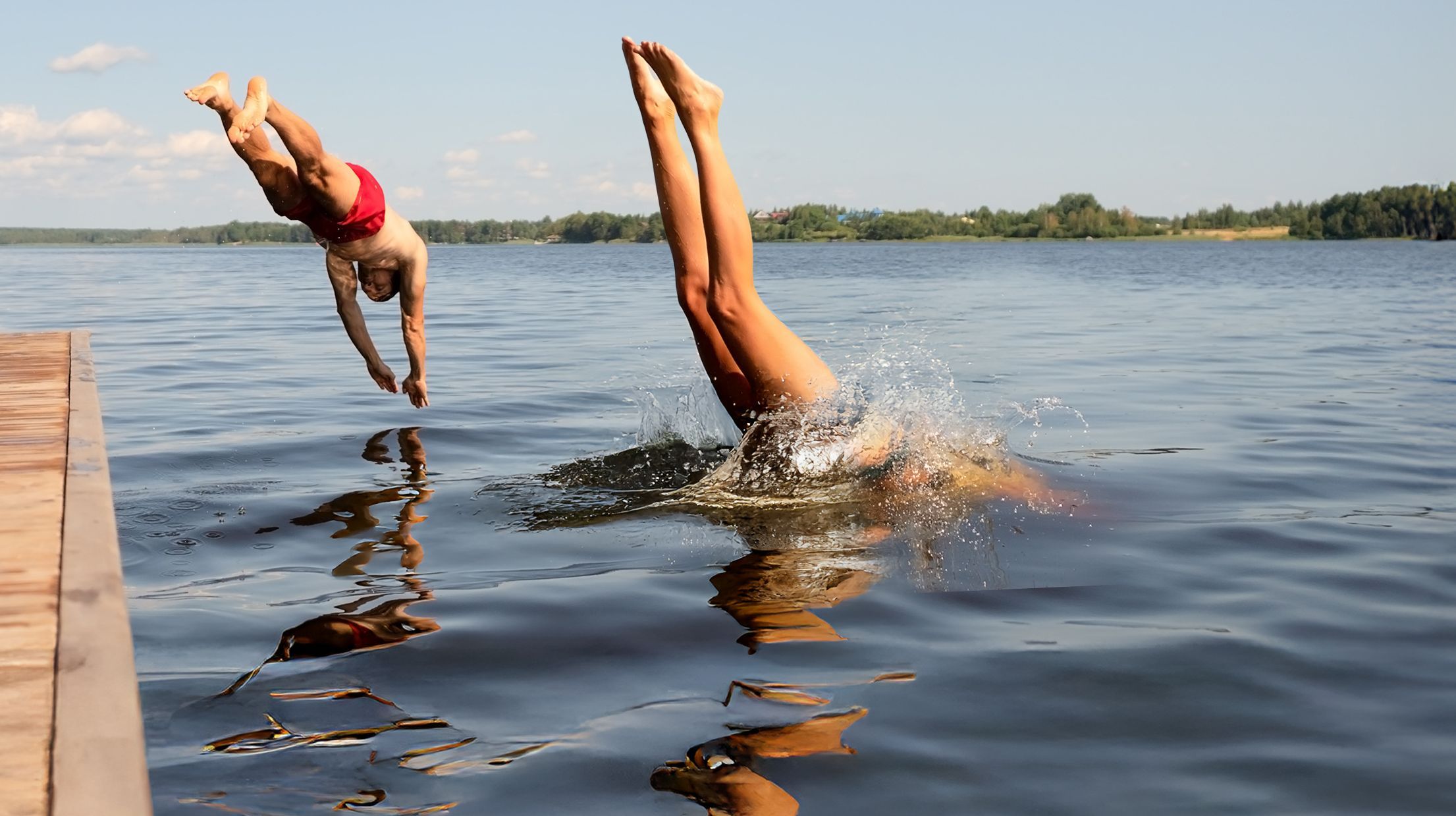 Eintauchen und geniessen – Sommerfreude pur Zwei Menschen springen kopfüber gleichzeitig von einem Steg in einen See an einem sonnigen Sommertag