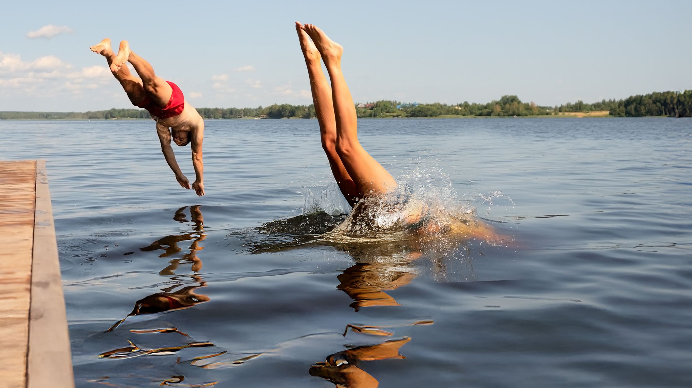 Eintauchen und geniessen – Sommerfreude pur Zwei Menschen springen kopfüber gleichzeitig von einem Steg in einen See an einem sonnigen Sommertag