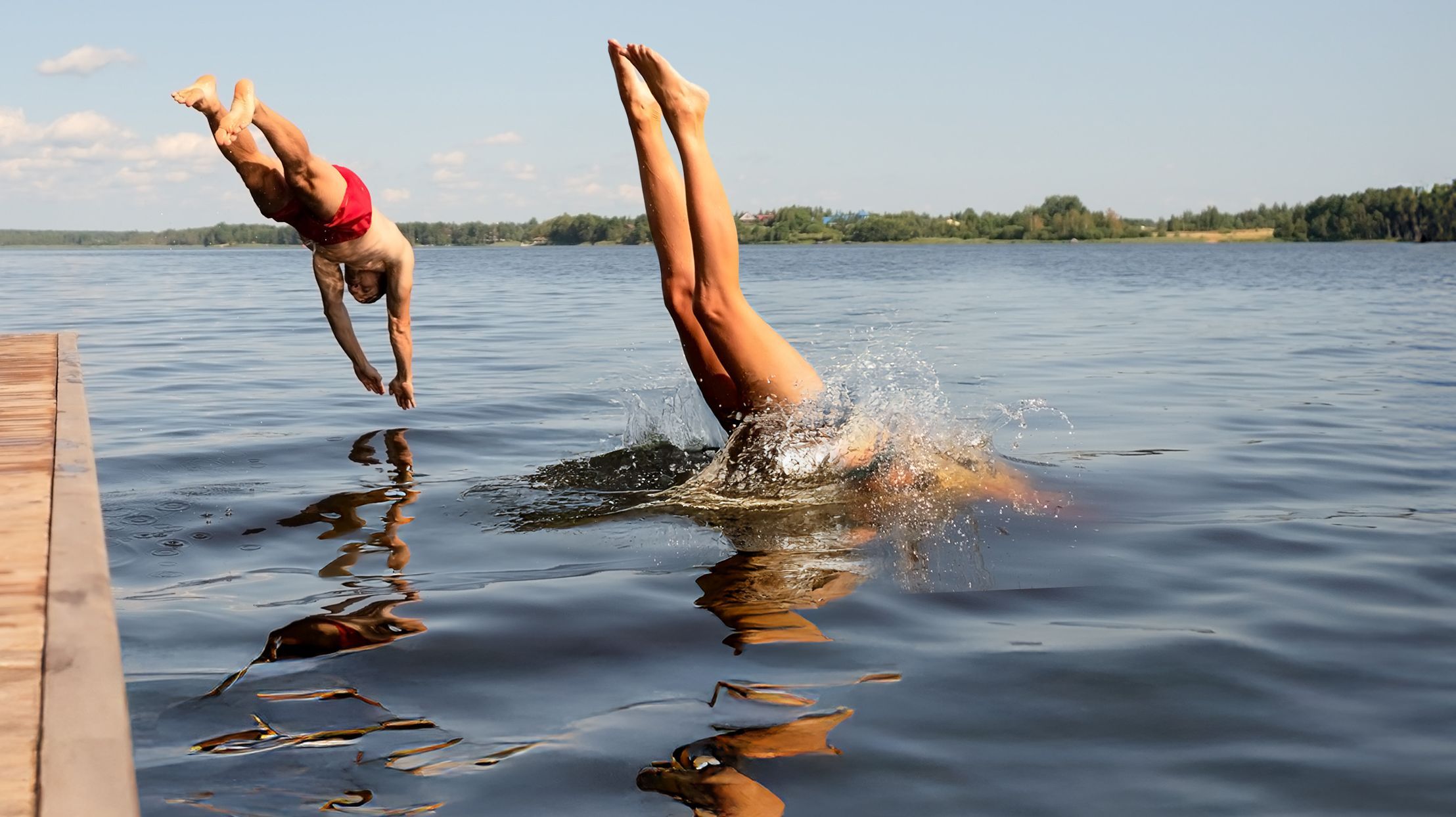 Eintauchen und geniessen – Sommerfreude pur Zwei Menschen springen kopfüber gleichzeitig von einem Steg in einen See an einem sonnigen Sommertag