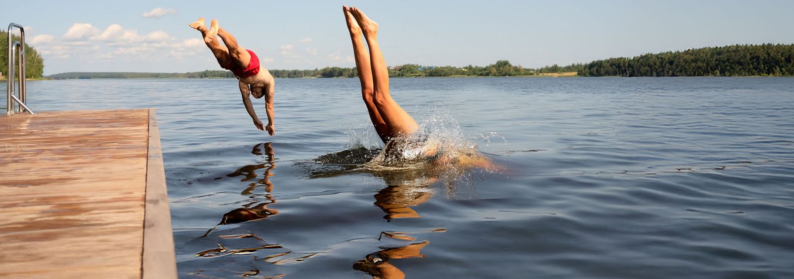 Zwei Menschen springen kopfüber gleichzeitig von einem Steg in einen See an einem sonnigen Sommertag