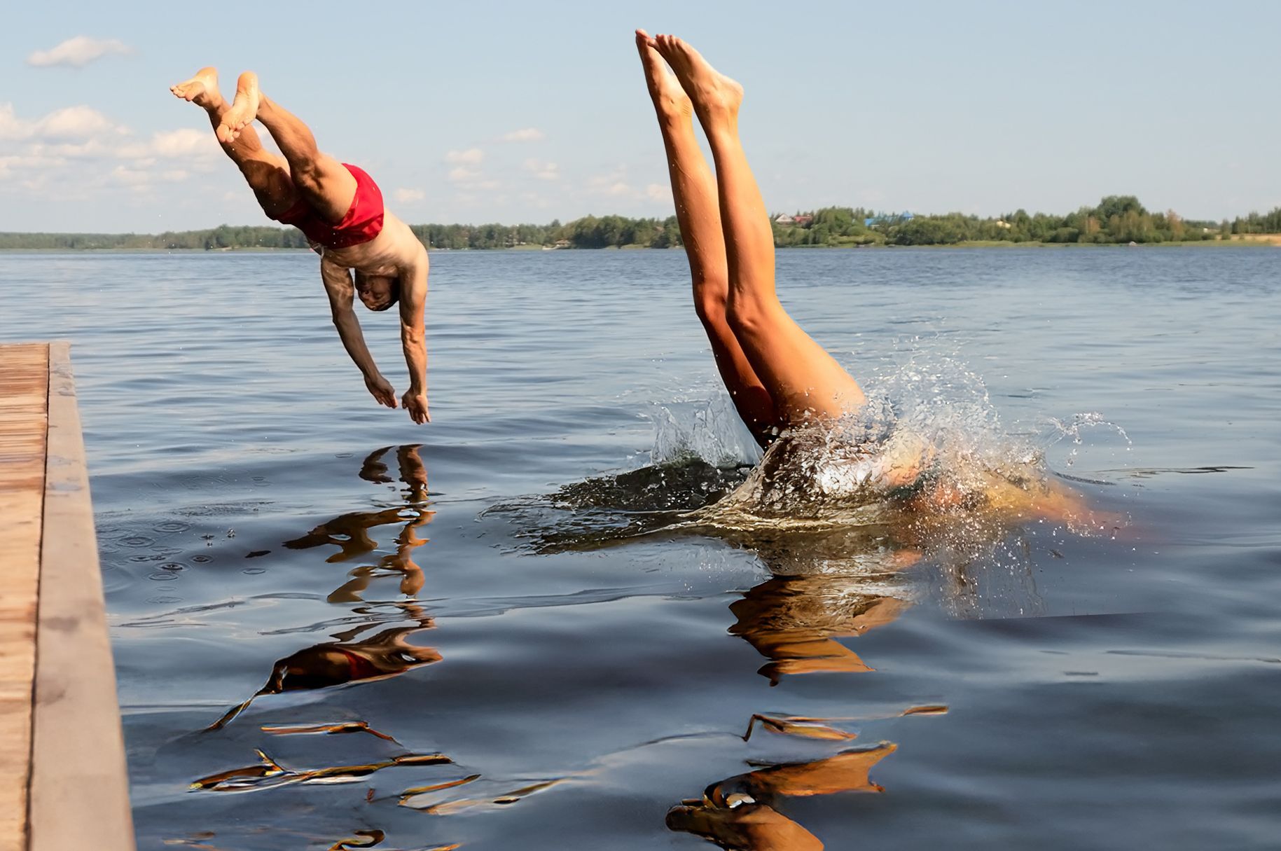 Eintauchen und geniessen – Sommerfreude pur Zwei Menschen springen kopfüber gleichzeitig von einem Steg in einen See an einem sonnigen Sommertag
