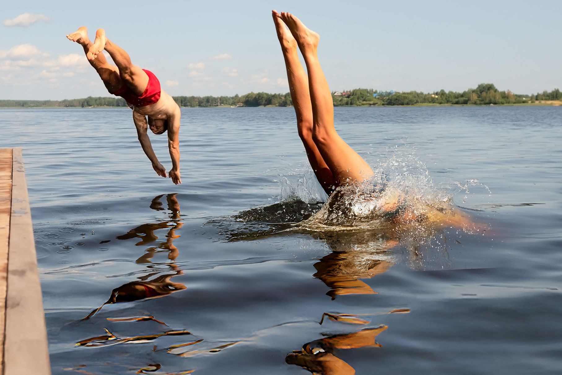 Eintauchen und geniessen – Sommerfreude pur Zwei Menschen springen kopfüber gleichzeitig von einem Steg in einen See an einem sonnigen Sommertag