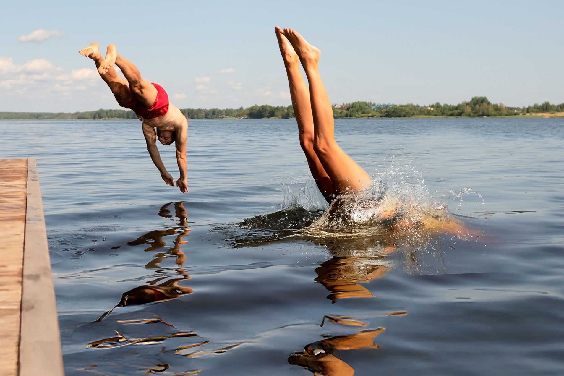 Eintauchen und geniessen – Sommerfreude pur Zwei Menschen springen kopfüber gleichzeitig von einem Steg in einen See an einem sonnigen Sommertag