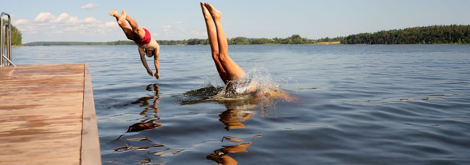 Zwei Menschen springen kopfüber gleichzeitig von einem Steg in einen See an einem sonnigen Sommertag