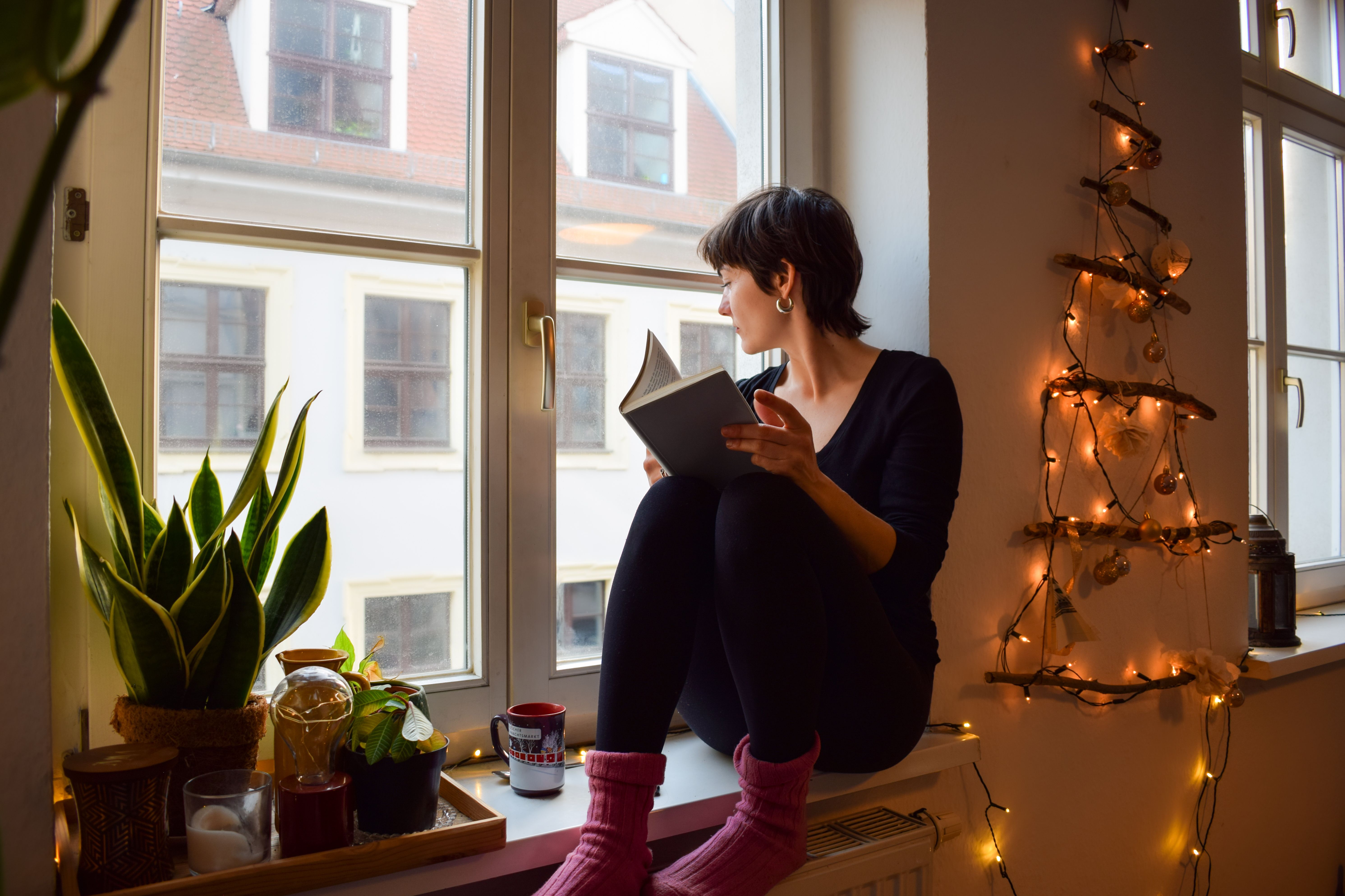 Frau sitzt mit dicken Kuschelsocken und einem Buch am Fenster