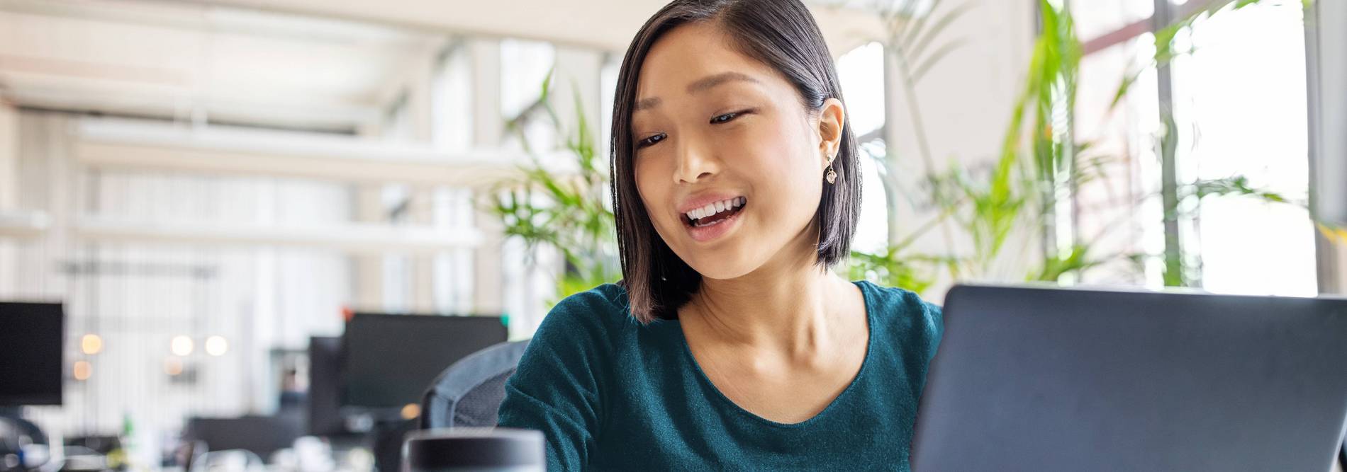 Asiatische Frau am Laptop spricht mit Alexa