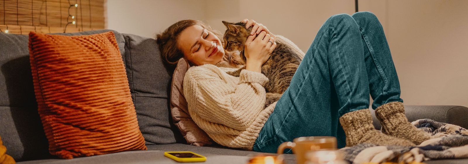 Junge Frau sitz gemütlich auf dem Sofa mit ihrer Katze.